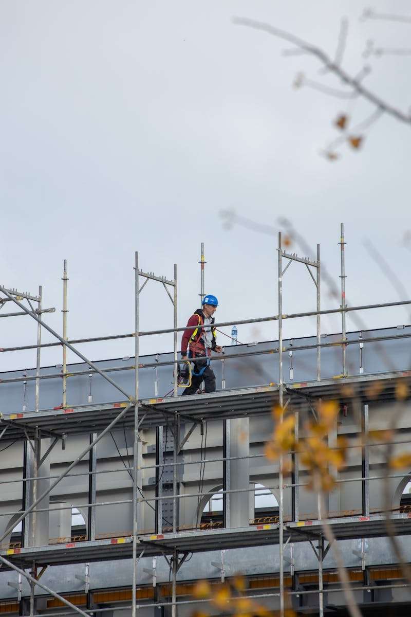 A construction worker walking on scaffolding at an outdoor building site.